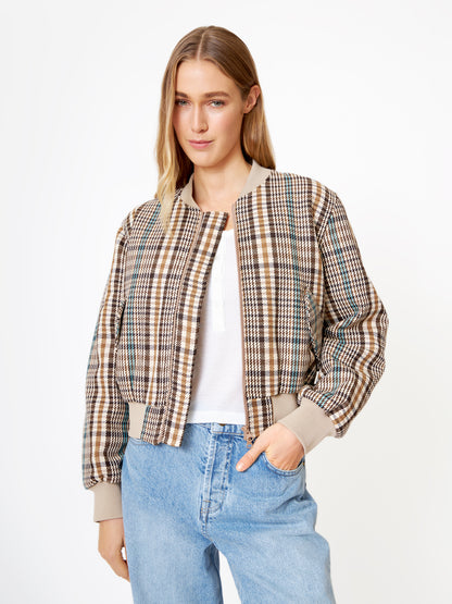 Eine Frau mit langen blonden Haaren trägt die Jacke Bomber Check über einem weißen Oberteil und hellblauen Jeans. Sie posiert vor einem schlichten weißen Hintergrund, hat eine Hand in der Tasche und schaut leicht lächelnd in die Kamera.