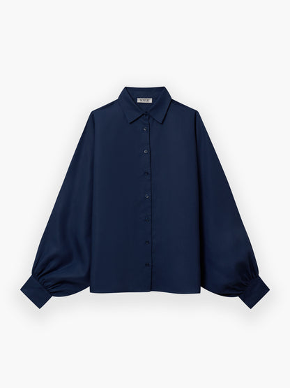 Die Bluse Antonia Slim Tencel Blue ist eine marineblaue Bluse mit langen, weiten Ärmeln, geknöpften Manschetten, einem klassischen Kragen und einer geknöpften Vorderseite, abgebildet auf einem einfarbig weißen Hintergrund.