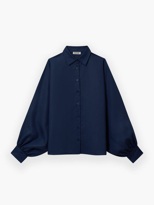 Die Bluse Antonia Slim Tencel Blue ist eine marineblaue Bluse mit langen, weiten Ärmeln, geknöpften Manschetten, einem klassischen Kragen und einer geknöpften Vorderseite, abgebildet auf einem einfarbig weißen Hintergrund.