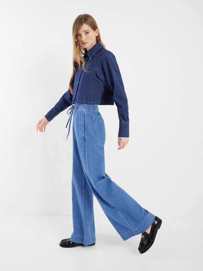 Eine Frau mit langem, glattem Haar trägt die dunkelblaue Jacke Hanna Denim und hellblaue Jeans mit weitem Bein für einen schicken Kombinationslook mit schwarzen Halbschuhen vor einem schlichten weißen Hintergrund.