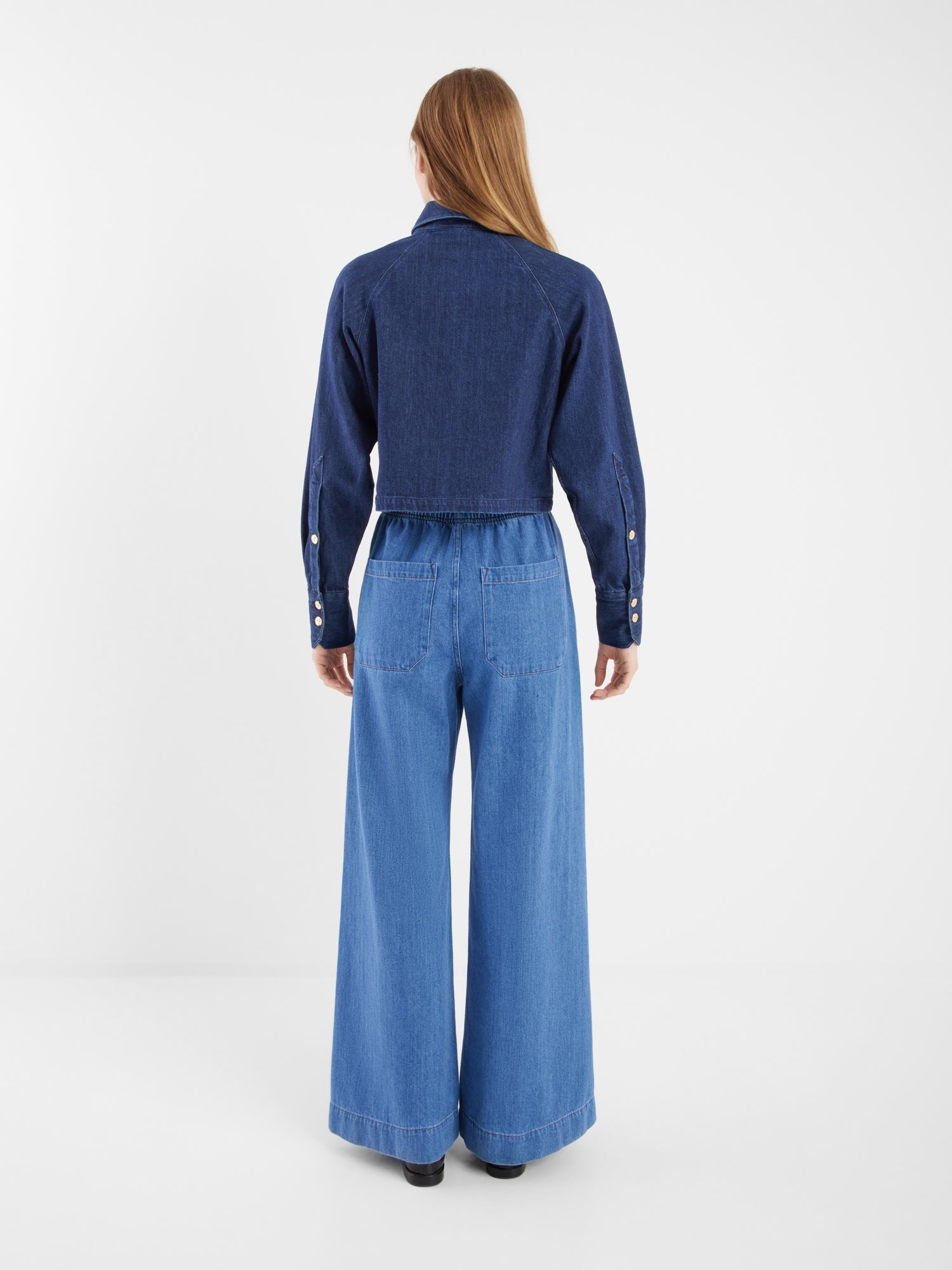 Eine Person mit langem, glattem Haar steht in der dunkelblauen Jacke Hanna Denim und hellblauen Jeans mit hoher Taille und weitem Bein für einen schicken Co-Ord-Look vor einem schlichten weißen Hintergrund.