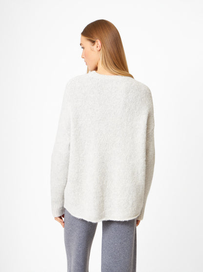 Eine Frau mit glattem, hellbraunem Haar steht mit dem Rücken zur Kamera. Sie trägt den Pullover LIV in Hellgrau und eine passende graue Hose vor einem schlichten weißen Hintergrund.