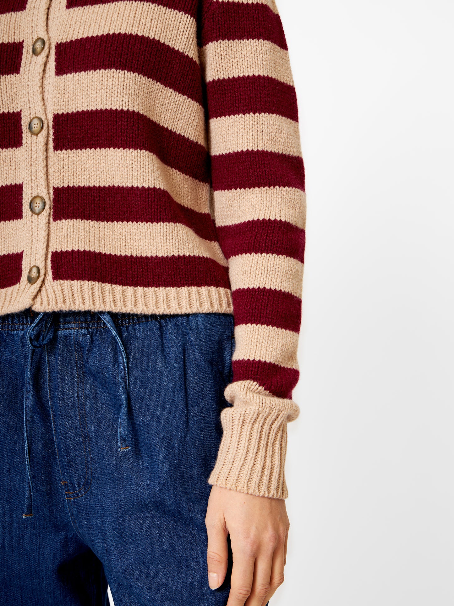 Eine Person, die von der Schulter bis zum Oberschenkel gezeigt wird, trägt eine blaue Hose mit Kordelzug und die Strickjacke Jacket Stripe Burgundy Stripe, wobei ein Arm entspannt an der Seite liegt, vor einem schlichten weißen Hintergrund.