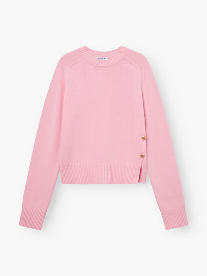 Der Pullover Rosa mit Goldknöpfen ist ein Damenpullover aus Merinowolle mit langen Ärmeln, gerippten Bündchen und Saum sowie zwei goldenen Zierknöpfen an der Taille.