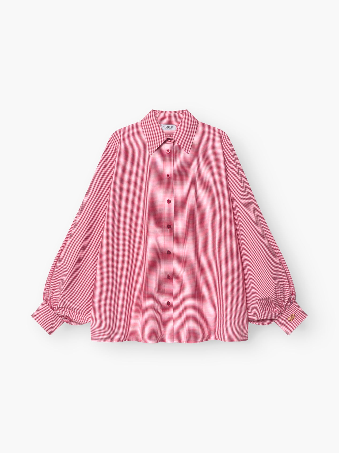 Die Bluse Antonia Brezel Red ist eine locker sitzende, langärmelige rosafarbene Bluse mit Halsausschnitt, Knopfleiste, Puffärmeln mit geknöpften Manschetten und einem kleinen gelben Etikett an einer Manschette.