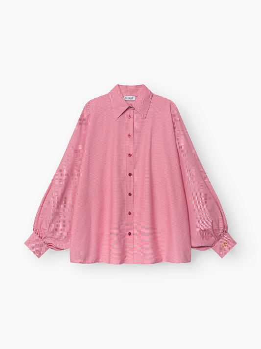 Die Bluse Antonia Brezel Red ist eine locker sitzende, langärmelige rosafarbene Bluse mit Halsausschnitt, Knopfleiste, Puffärmeln mit geknöpften Manschetten und einem kleinen gelben Etikett an einer Manschette.