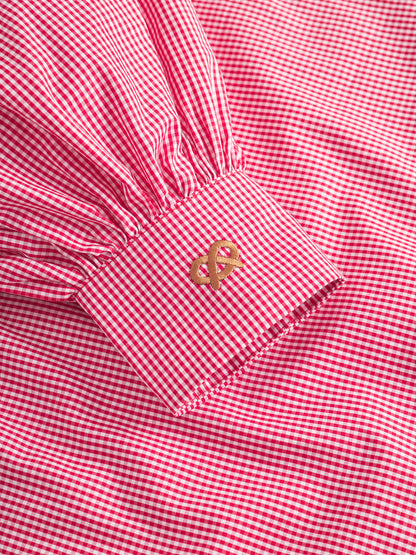 Eine Nahaufnahme des roten Ärmels der Bluse Antonia Brezel, die die rot-weiß karierte Manschette mit goldener Symbolstickerei hervorhebt.
