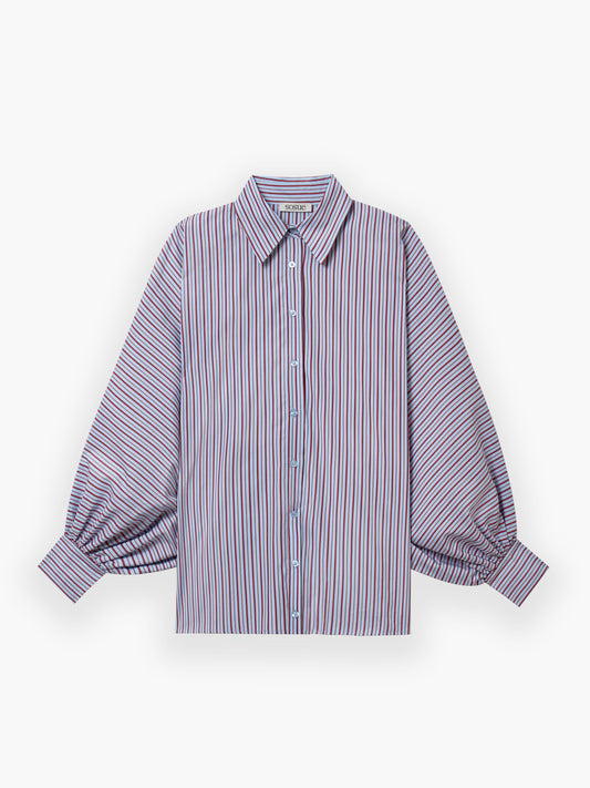 Die Bluse Antonia Blue Burgundy Stripe zeigt rote, blaue und weiße Streifen, hat lange Ärmel, Knopfleiste, spitze Kragen sowie weite Manschetten. Oversize-Schnitt und flach auf weißem Hintergrund präsentiert.