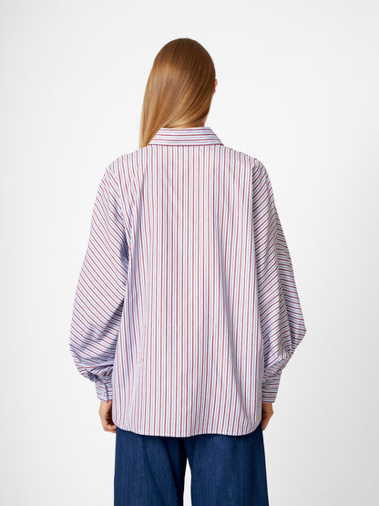 Eine Person mit langen glatten Haaren, von hinten gesehen, trägt die Bluse Antonia Blue Burgundy Stripe und eine dunkelblaue Hose. Der Hintergrund ist einfarbig weiß.