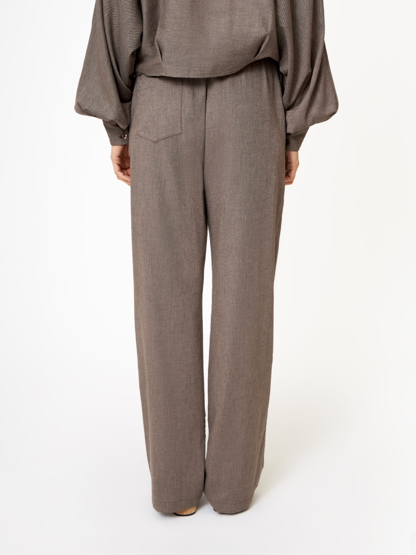 Eine Person schaut weg und zeigt nur die untere Hälfte in einer gemütlichen Winter-Streetstyle-Hose in Flanell Taupe vor einem schlichten weißen Hintergrund.