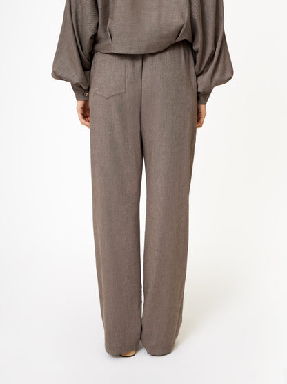 Eine Person schaut weg und zeigt nur die untere Hälfte in einer gemütlichen Winter-Streetstyle-Hose in Flanell Taupe vor einem schlichten weißen Hintergrund.