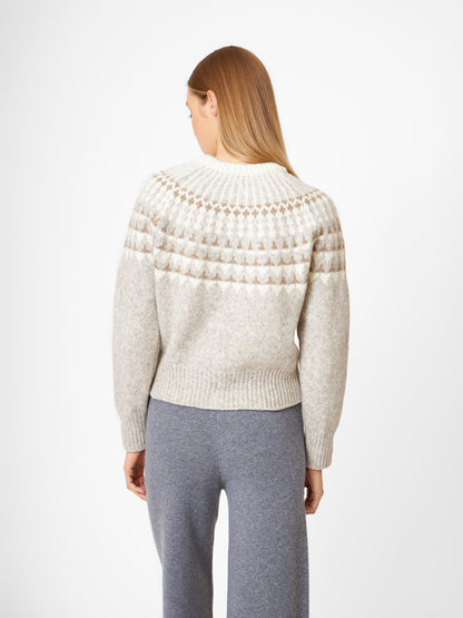 Eine Person mit langem, glattem blondem Haar steht mit dem Rücken zur Kamera und trägt eine hellgraue Jacke Norweger Vol II Greige mit einer gemusterten Passe und einer grauen Hose vor einem schlichten weißen Hintergrund.