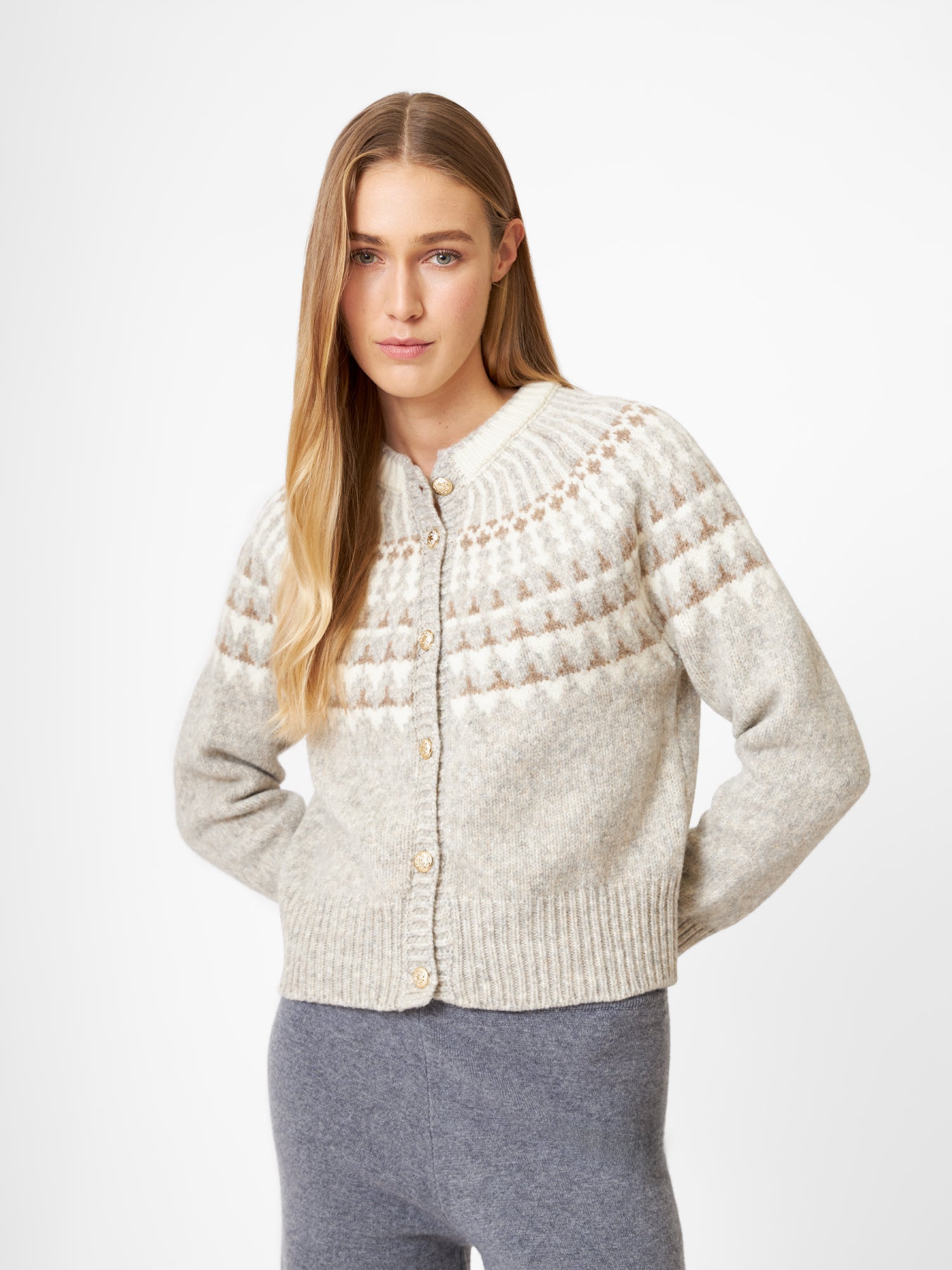 Eine Frau mit langen blonden Haaren trägt die Jacke Norweger Vol II Greige mit Knöpfen und einer grauen Hose, die vor einem schlichten weißen Hintergrund steht.