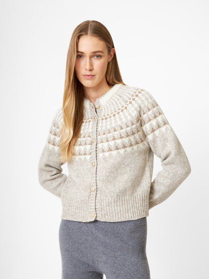 Eine Frau mit langen blonden Haaren trägt die Jacke Norweger Vol II Greige mit Knöpfen und einer grauen Hose, die vor einem schlichten weißen Hintergrund steht.