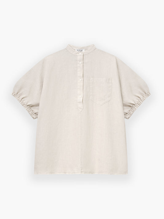 Das Cowboy Button Linen Beige ist ein locker sitzendes, hellbeiges Kurzarmhemd mit Mandarinenkragen, Teilknopfleiste, Brusttasche und gerafften Ärmelsäumen auf weißem Grund.