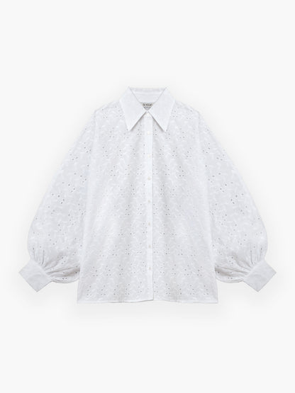 Die Bluse „Antonia Lace White“ ist eine weiße, langärmelige Bluse aus leichter weißer Baumwollspitze mit zarter Lochstickerei. Diese elegante, oversized Sommerbluse für Damen verfügt über einen spitzen Kragen und eine Knopfleiste vorne sowie Puffärmel mit Manschetten an den Handgelenken, die dem raffinierten Design eine luftige Note verleihen. Die Bluse wird vor einem weißen Hintergrund präsentiert.