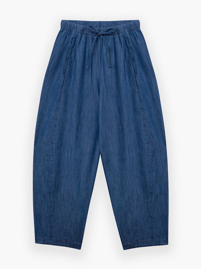 Die Lizzy Denim Hose ist locker geschnitten, hat einen elastischen Bund mit Kordelzug und ist aus leichtem Denim gefertigt. Diese übergroße Hose mit weitem Bein ist flach auf weißem Grund abgebildet.