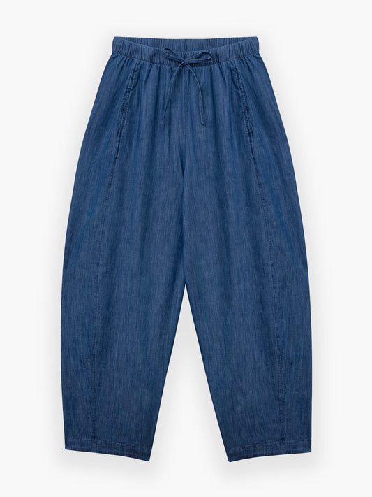 Die Lizzy Denim Hose ist locker geschnitten, hat einen elastischen Bund mit Kordelzug und ist aus leichtem Denim gefertigt. Diese übergroße Hose mit weitem Bein ist flach auf weißem Grund abgebildet.