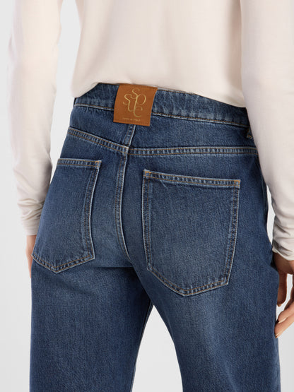 Eine Person ist von hinten zu sehen. Sie trägt ein helles Langarmhemd und dazu die NOLA Jeans Dark Blue – Wide Leg Damenjeans, die aus hochwertigem Denim gefertigt ist und somit Komfort und Langlebigkeit bietet. Dieses Modell verfügt über zwei Gesäßtaschen und ein braunes Lederaufnäher mit geprägter Schrift am Bund.