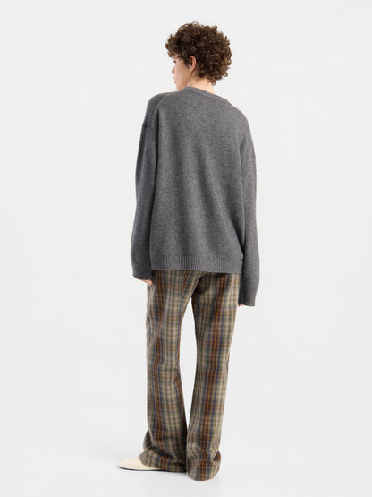 Eine Person mit lockigem Haar steht mit dem Rücken zur Kamera und trägt einen lockeren grauen Pullover sowie die Hose „Karoline Check“. Der schlichte weiße Hintergrund unterstreicht das lässige Outfit.