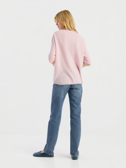 Eine Person steht mit dem Rücken zur Kamera und trägt das Strick-T-Shirt „Aurora Rose“, eine blaue Jeans und blaue Schuhe vor einem schlichten weißen Hintergrund.