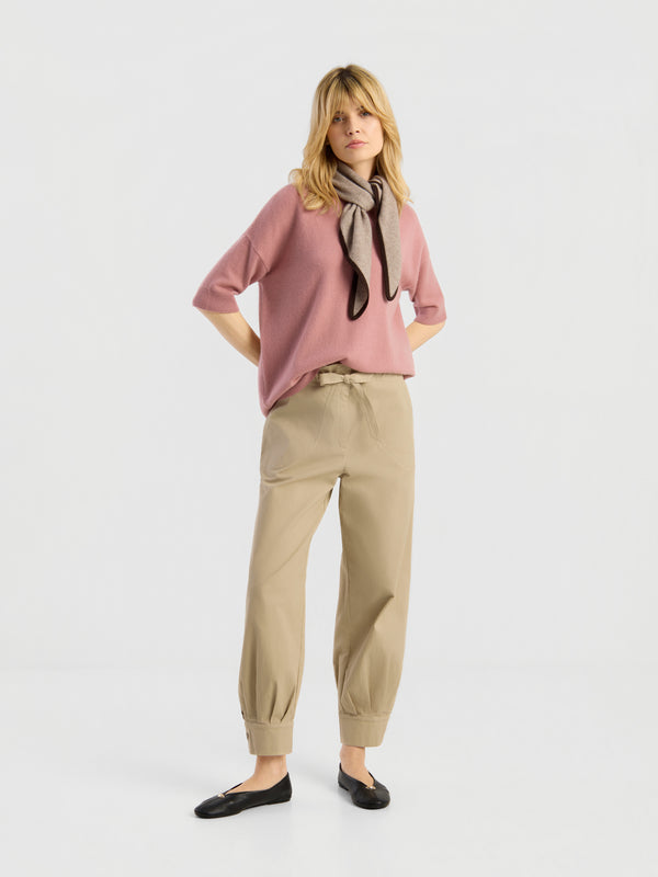 Eine Frau steht mit den Händen in den Taschen da; sie trägt „Blush & Beige“, schwarze Ballerinas und einen grauen Schal; der Hintergrund ist schlicht weiß.