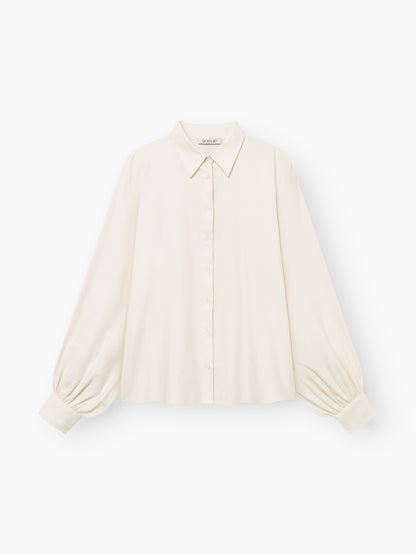 Die Bluse „Antonia Flanell Offwhite“ ist cremefarben, langärmelig und verfügt über einen spitzen Kragen, eine Knopfleiste vorne sowie geraffte Ärmelbündchen. Sie ist aus leichtem Stoff gefertigt und besticht durch eine lockere Passform und eine leicht kastenförmige Silhouette.