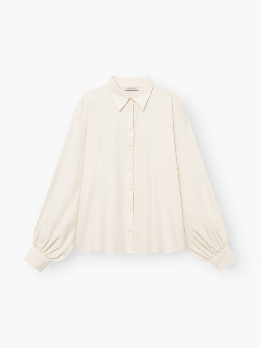 Die Bluse „Antonia Flanell Offwhite“ ist cremefarben, langärmelig und verfügt über einen spitzen Kragen, eine Knopfleiste vorne sowie geraffte Ärmelbündchen. Sie ist aus leichtem Stoff gefertigt und besticht durch eine lockere Passform und eine leicht kastenförmige Silhouette.