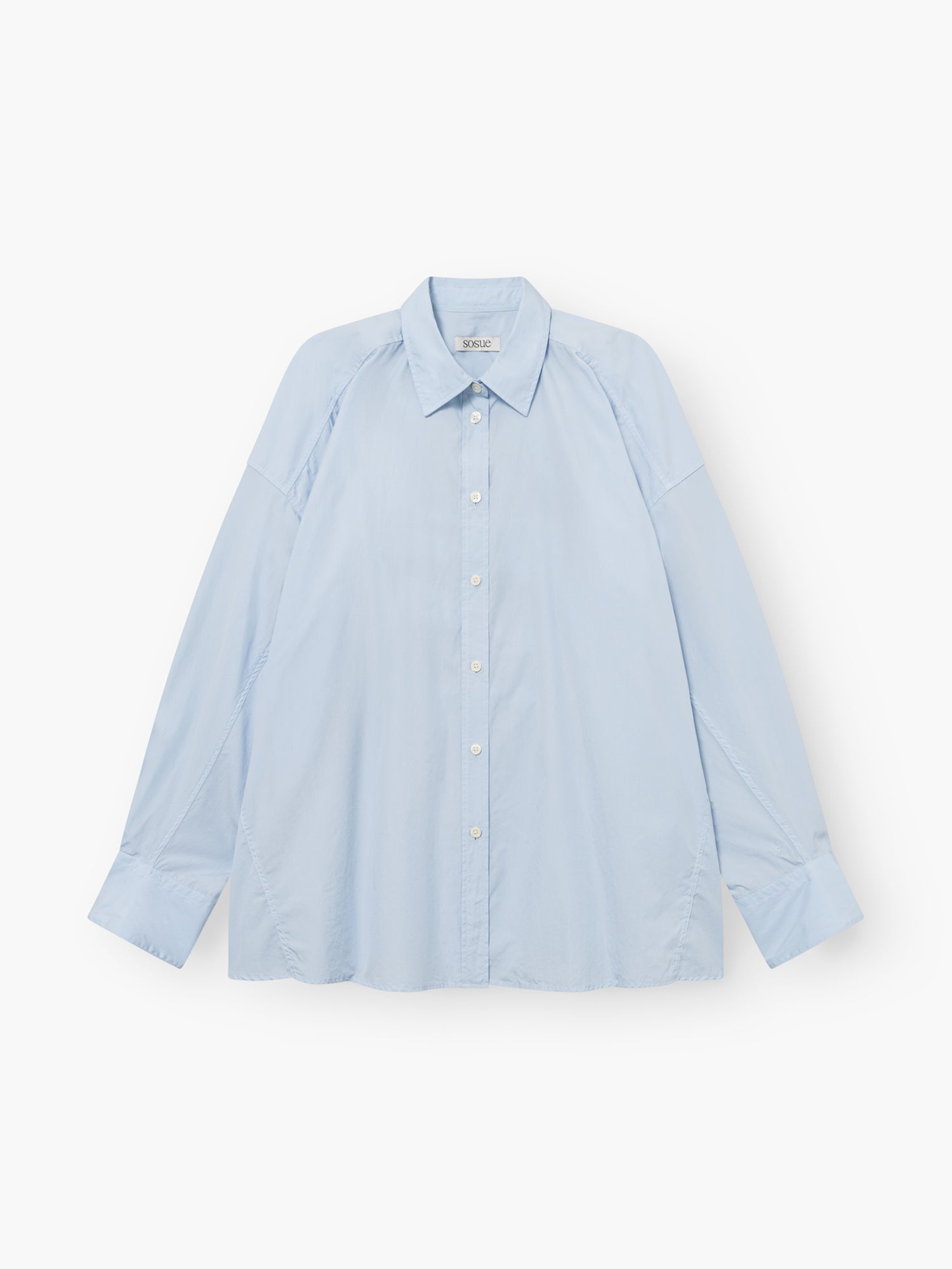 Die Bluse „Hannah Lightblue“ ist ein hellblaues, langärmeliges Oberteil mit Kragen und Knopfleiste in Oversize-Passform sowie weißen Knöpfen auf der Vorderseite, das flach auf einem weißen Hintergrund abgebildet ist.