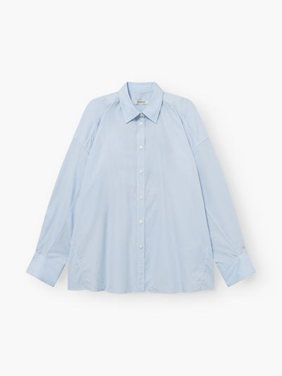Die Bluse „Hannah Lightblue“ ist ein übergroßes, hellblaues Langarmhemd mit Kragen und Knopfleiste, das flach auf weißem Hintergrund abgebildet ist. Dieser lässige Schnitt besticht durch sichtbare Nähte an den Seiten und Schultern, die für zusätzliche Akzente sorgen. Hergestellt in Portugal aus 100 % Baumwolle, bietet sie außergewöhnlichen Tragekomfort und höchste Qualität.