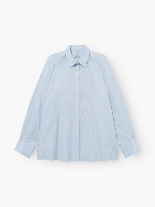 Die Bluse „Hannah Lightblue“ ist ein übergroßes, hellblaues Langarmhemd mit Kragen und Knopfleiste, das flach auf weißem Hintergrund abgebildet ist. Dieser lässige Schnitt besticht durch sichtbare Nähte an den Seiten und Schultern, die für zusätzliche Akzente sorgen. Hergestellt in Portugal aus 100 % Baumwolle, bietet sie außergewöhnlichen Tragekomfort und höchste Qualität.