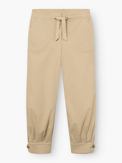 Beigefarbene „Love Pants“ mit Vordertaschen, einem Kordelzug am Bund und geknöpften Bündchen an den Knöcheln, flach auf einem weißen Hintergrund liegend.