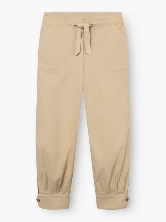 Beigefarbene „Love Pants“ mit Vordertaschen, einem Kordelzug am Bund und geknöpften Bündchen an den Knöcheln, flach auf einem weißen Hintergrund liegend.