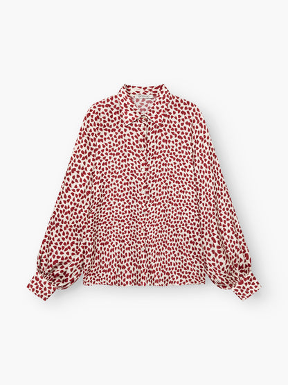 Die Bluse „Antonia Valentine“ ist ein locker sitzendes, langärmeliges Hemd mit Kragen, weiten Ärmeln mit Manschetten und einem weißen Grund, der mit einem durchgehenden roten Herzmuster verziert ist.