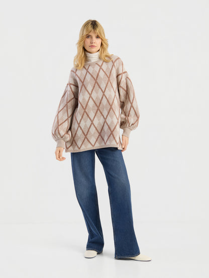 Eine Person, die den Pullover „Antonia Diamond“ trägt – einen beigen Pullover mit Rautenmuster und Ballonärmeln –, kombiniert mit einem hellen Rollkragenpullover, einer blau-weit geschnittenen Jeans und weißen Schuhen, steht vor einem schlichten weißen Hintergrund.