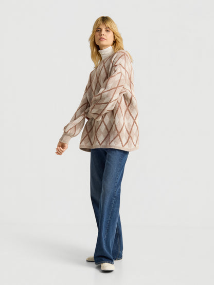 Eine Frau, die den Pullover „Antonia Diamond“ mit einem beige-braunen Rautenmuster trägt, kombiniert mit einer blauen Jeans mit weitem Bein und weißen Schuhen, steht vor einem schlichten weißen Hintergrund.