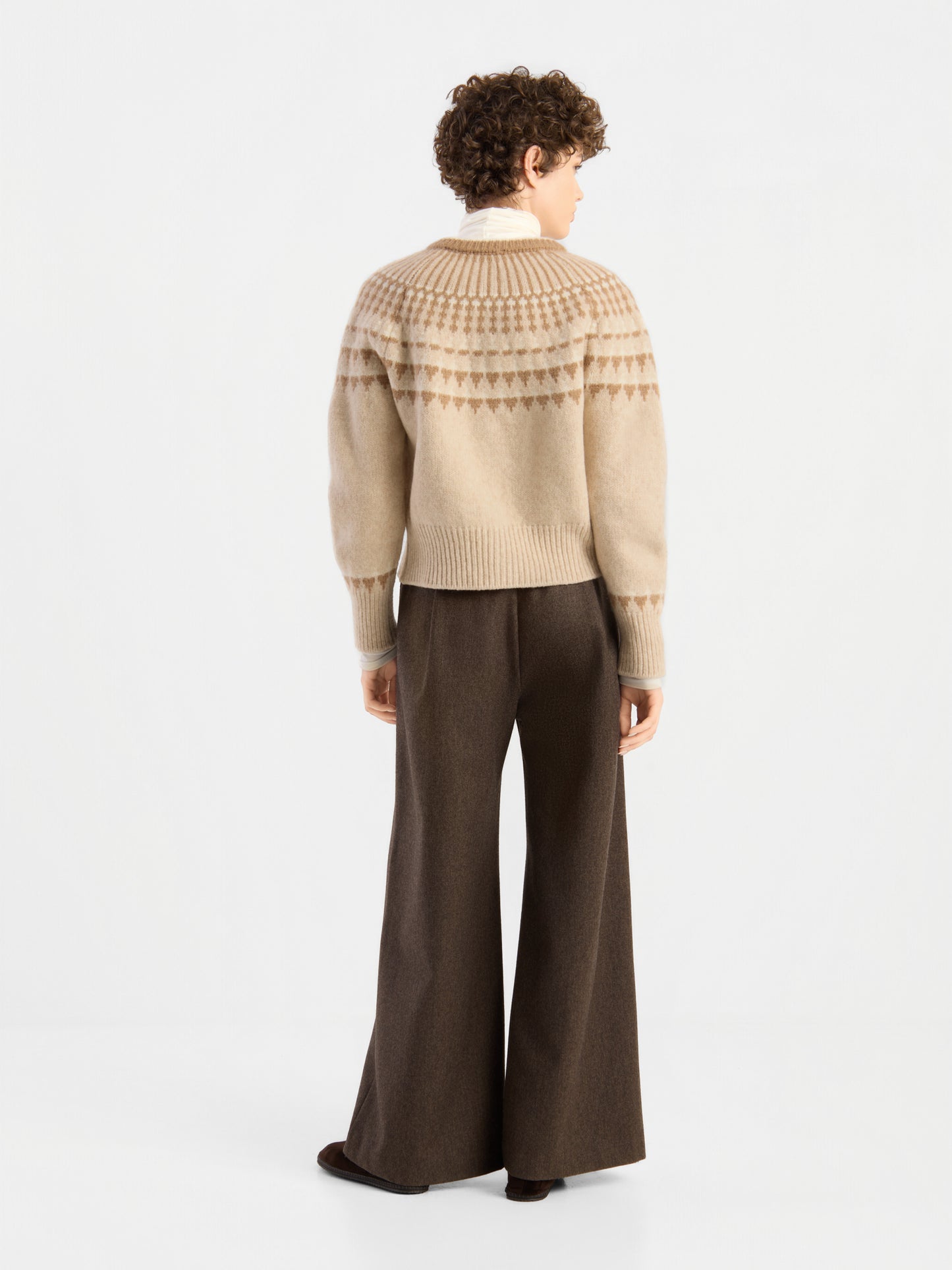 Eine Person mit kurzen Locken und einer braunen Hose mit weitem Bein steht mit dem Rücken zur Kamera vor einem schlichten weißen Hintergrund und trägt die „Norweger Jacket Vol. 3“.