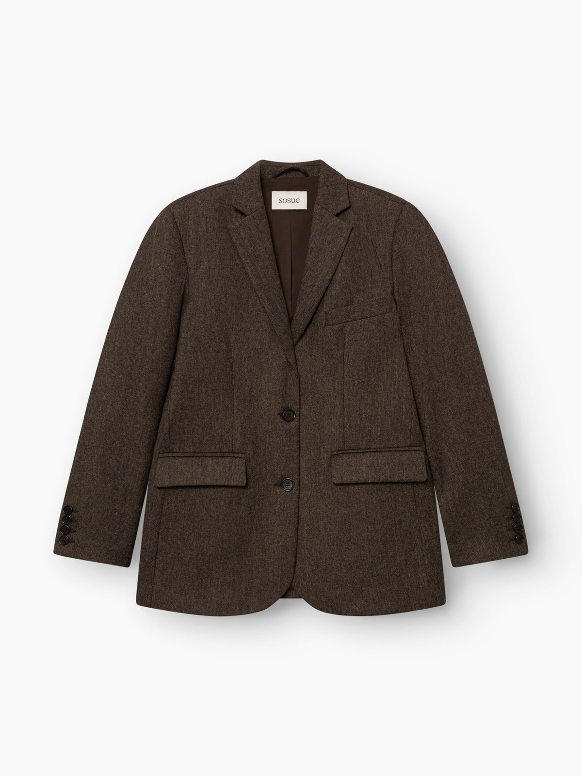 Der Blazer „Karoline Braun“ ist ein taillierter Blazer mit fallendem Revers, zwei Knöpfen, einer Brusttasche und zwei Pattentaschen vorne. Er ist aus weichem Baumwollflanell gefertigt, was ihm eine edle Optik verleiht. Das Modell wird in Portugal hergestellt und hier flach auf einem weißen Hintergrund präsentiert.