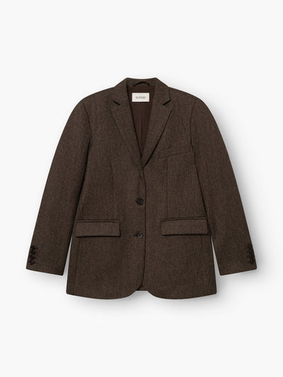 Der Blazer „Karoline Braun“ ist ein taillierter Blazer mit fallendem Revers, zwei Knöpfen, einer Brusttasche und zwei Pattentaschen vorne. Er ist aus weichem Baumwollflanell gefertigt, was ihm eine edle Optik verleiht. Das Modell wird in Portugal hergestellt und hier flach auf einem weißen Hintergrund präsentiert.