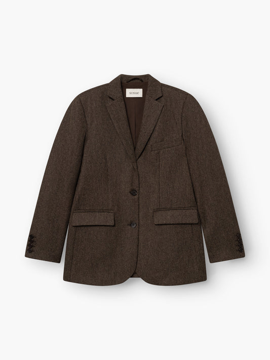 Der Blazer „Karoline Braun“ ist ein taillierter Blazer mit fallendem Revers, zwei Knöpfen, einer Brusttasche und zwei Pattentaschen vorne. Er ist aus weichem Baumwollflanell gefertigt, was ihm eine edle Optik verleiht. Das Modell wird in Portugal hergestellt und hier flach auf einem weißen Hintergrund präsentiert.