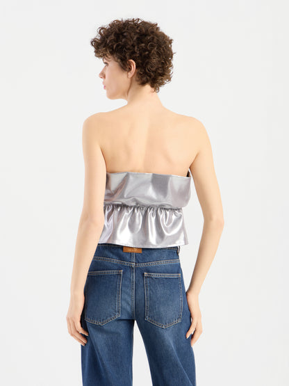 Eine Person mit kurzen Locken trägt ein „Pleat Top Silber“ und eine blaue Jeans und steht mit dem Rücken zur Kamera vor einem schlichten weißen Hintergrund.