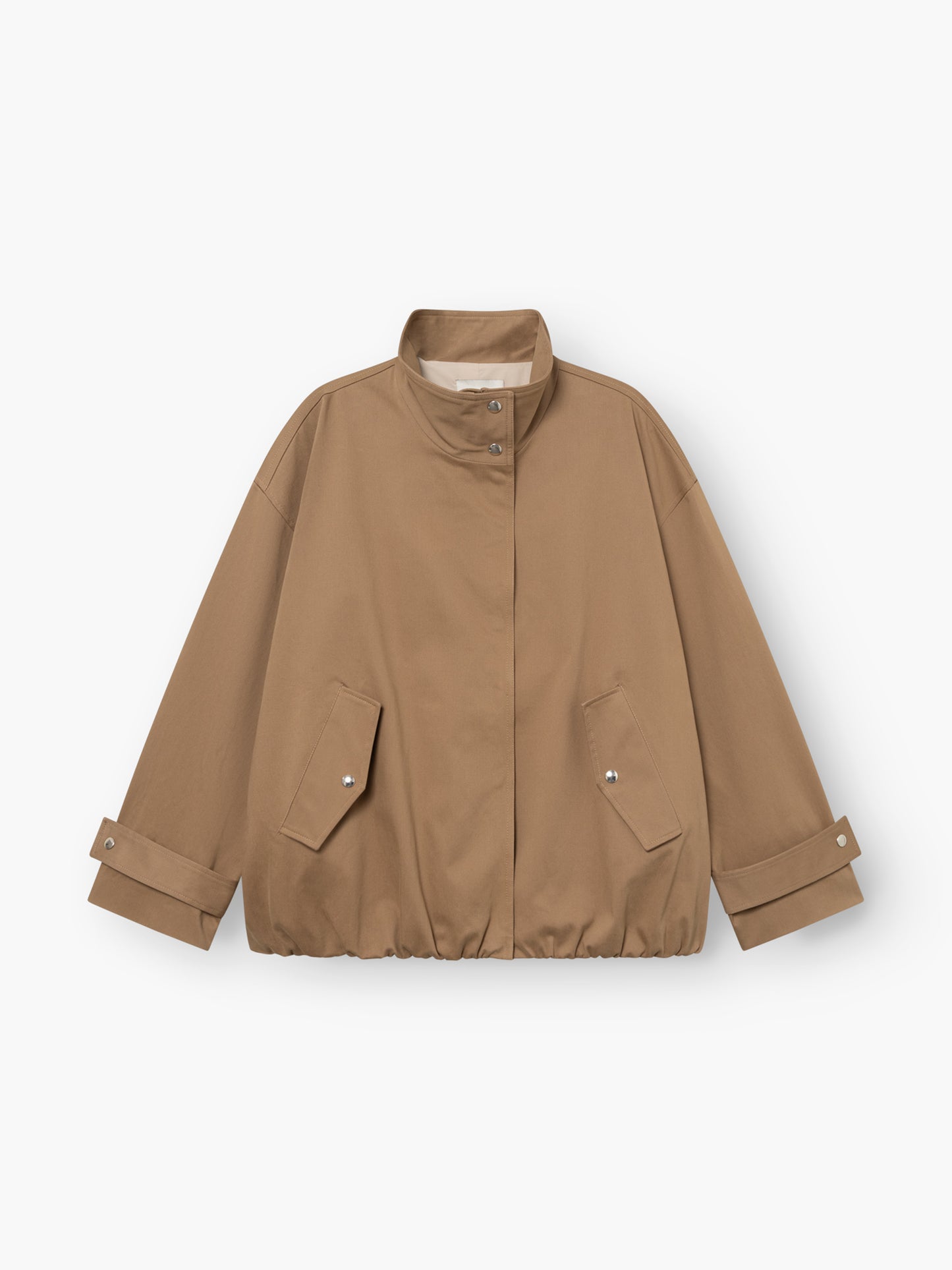 Eine hellbraune, locker sitzende „Jacke Hamptons“ – eine Damen-Übergangsjacke mit Stehkragen, Druckknopfleiste vorne, zwei Pattentaschen und verstellbaren Ärmelbündchen. Der Saum ist leicht gerafft. Diese im Utility-Stil gehaltene Jacke ist flach auf einem weißen Hintergrund ausgelegt.