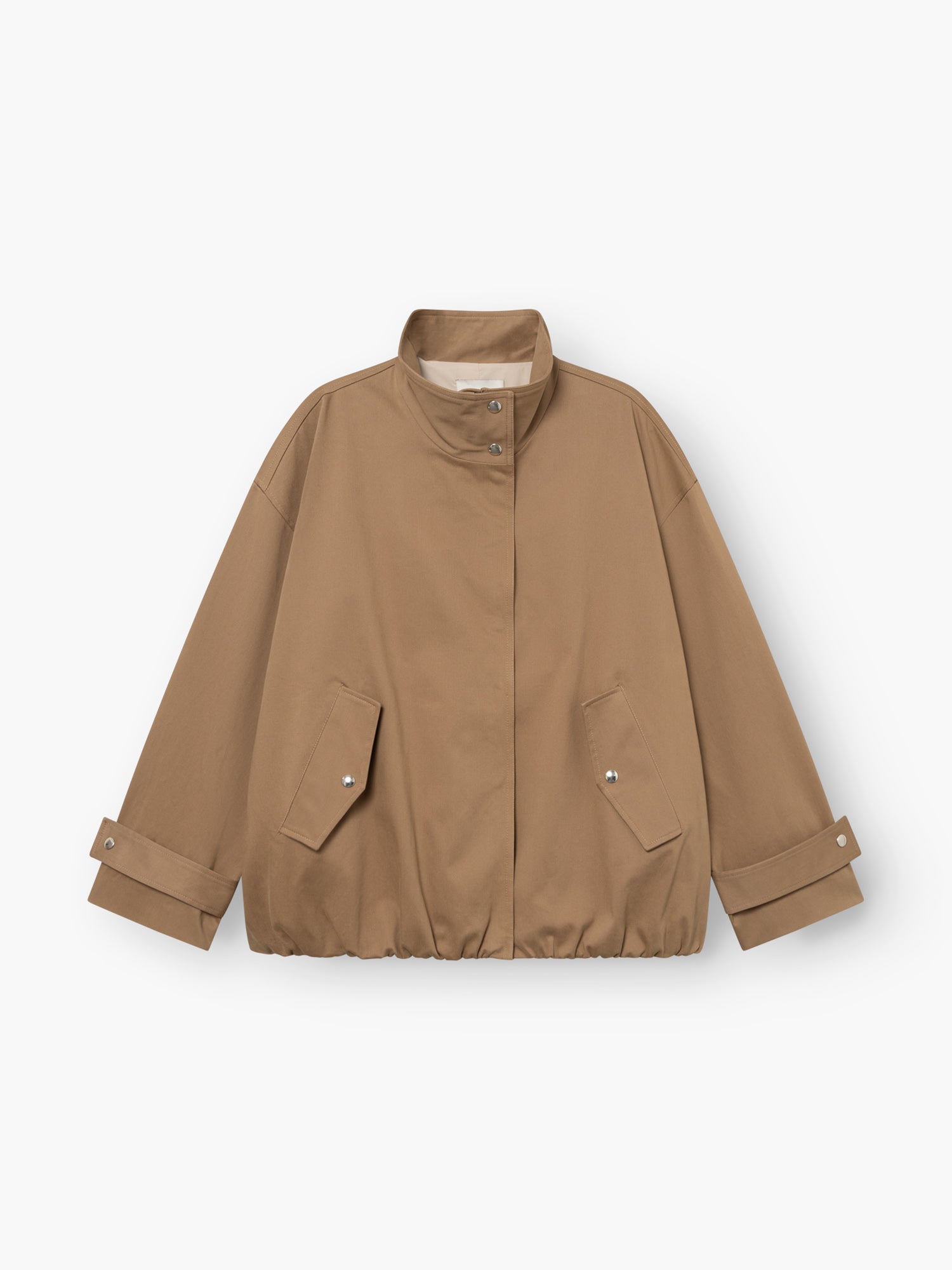 Eine hellbraune, locker sitzende „Jacke Hamptons“ – eine Damen-Übergangsjacke mit Stehkragen, Druckknopfleiste vorne, zwei Pattentaschen und verstellbaren Ärmelbündchen. Der Saum ist leicht gerafft. Diese im Utility-Stil gehaltene Jacke ist flach auf einem weißen Hintergrund ausgelegt.