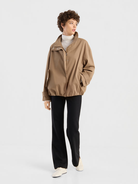 Vor einem schlichten weißen Hintergrund präsentiert ein Model den „Ready for Fall“-Look: eine hellbraune Oversize-Jacke über einem weißen Rollkragenpullover, dazu eine schwarze Hose und weiße Schuhe.