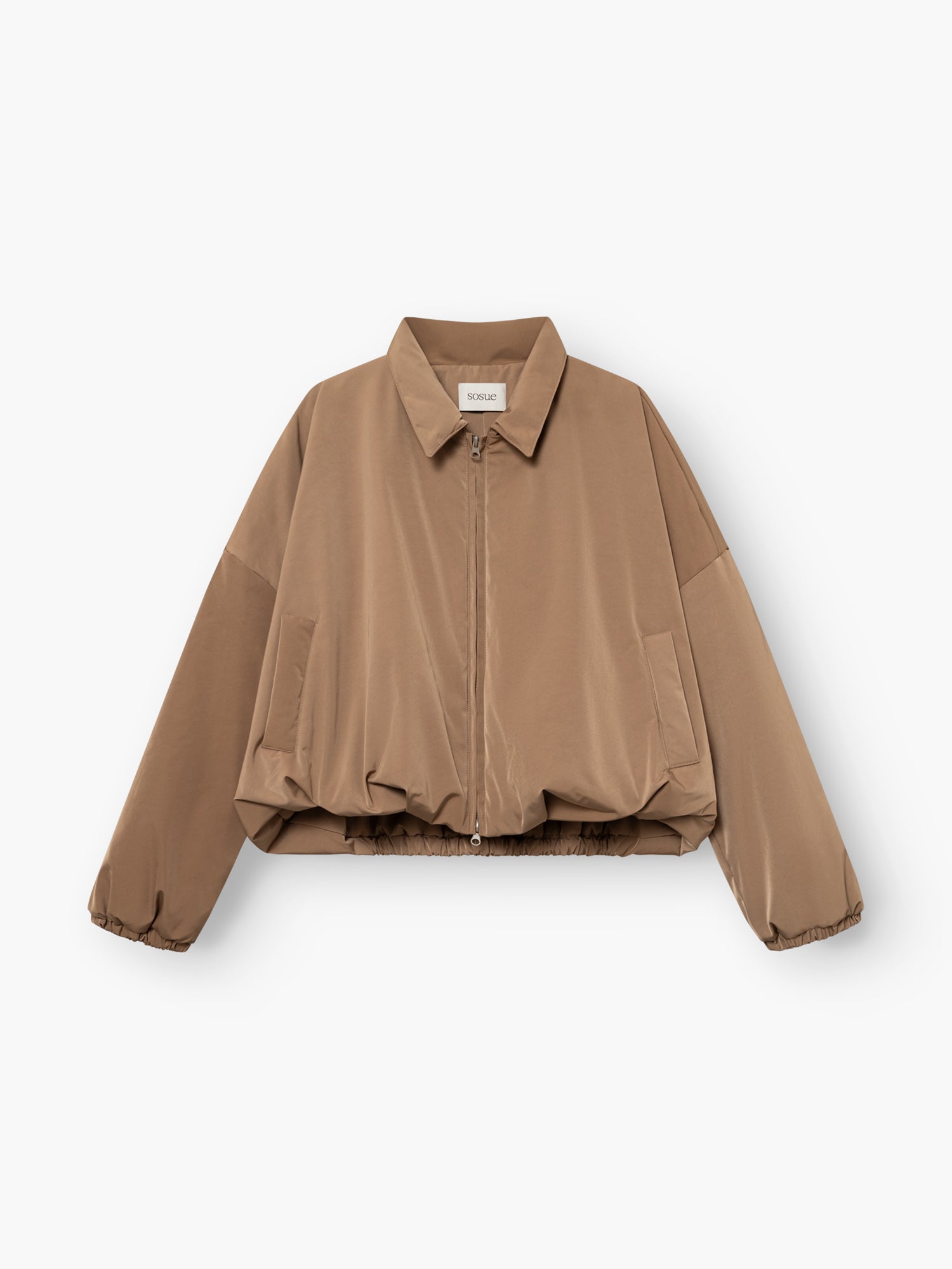 Die „Ballon Jacket“ ist eine hellbraune, langärmelige, kurz geschnittene Jacke mit Reißverschluss vorne, Hemdkragen, Seitentaschen und elastischem Saum, die flach auf einem weißen Hintergrund abgebildet ist.
