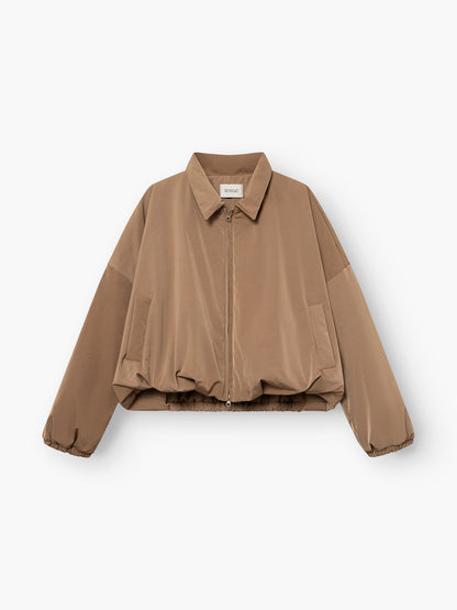 Die „Ballon Jacket“ ist eine hellbraune, langärmelige, kurz geschnittene Jacke mit Reißverschluss vorne, Hemdkragen, Seitentaschen und elastischem Saum, die flach auf einem weißen Hintergrund abgebildet ist.