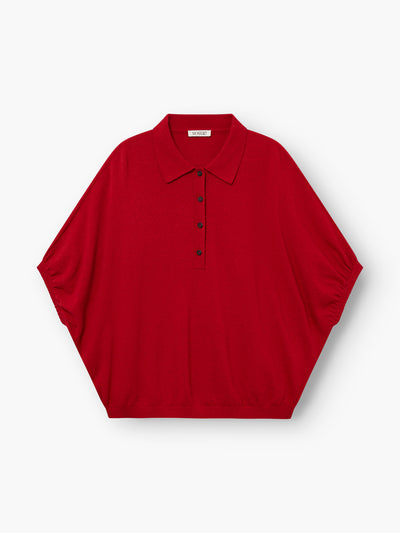 Das „Cowboy Polo Knit Red“ ist ein locker sitzendes, kurzärmeliges Polohemd mit spitzem Kragen und fünf schwarzen Knöpfen auf der Vorderseite, abgebildet auf einem schlichten weißen Hintergrund.
