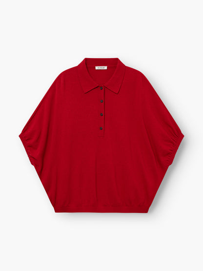 Das „Cowboy Polo Knit Red“ ist ein locker sitzendes, kurzärmeliges Polohemd mit spitzem Kragen und fünf schwarzen Knöpfen auf der Vorderseite, abgebildet auf einem schlichten weißen Hintergrund.