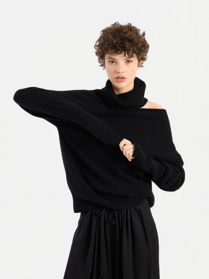 Eine Frau mit kurzen Locken trägt den Pullover „Scaya Schwarz“, einen eleganten schwarzen Rollkragenpullover, und zieht ihren Ärmel zurecht, wobei sie einen Arm quer über den Körper hebt – vor einem schlichten weißen Hintergrund.