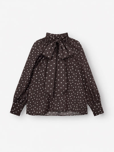 Die Bluse „Dotty Bow Brown Ecru“ ist eine dunkelbraune Langarmbluse aus Baumwoll-Voile mit weißen Polka-Punkten, die sich durch einen hohen Ausschnitt und eine große, am Kragen gebundene Schleife auszeichnet. Diese elegante Damenbluse in Braun/Ecru hat an den Ärmelbündchen geraffte Ärmel, die für einen dezenten Puff-Effekt sorgen, und wird in Italien hergestellt. Das Kleidungsstück wird vor einem weißen Hintergrund präsentiert.